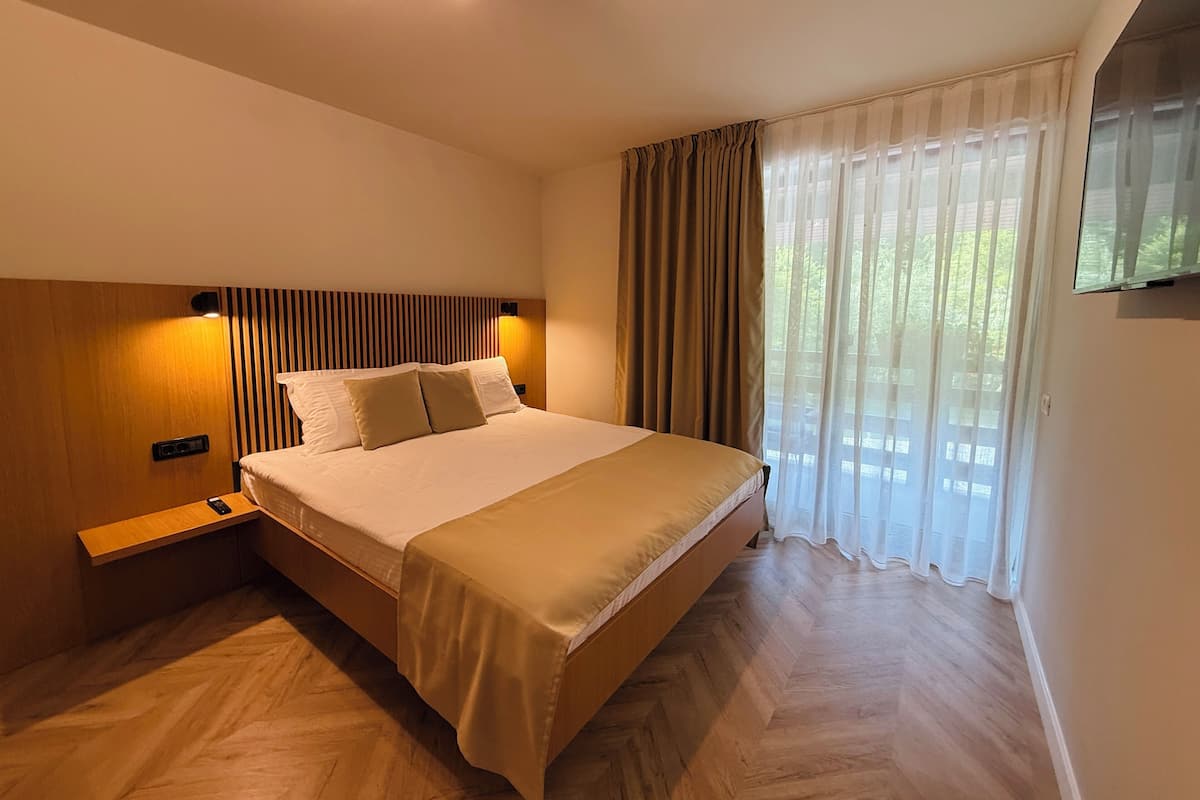 Une chambre moderne avec un grand lit, une tête de lit en bois, des tables de chevet et un téléviseur fixé au mur.