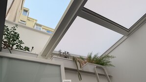 A skylight in a room with a view of neighboring buildings and some indoor plants. - Vimini Like a Local (Bari)