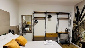 A hotel room with a bed, two pillows, a desk with a chair, a mirror, and a wall with a tropical mural. - Vimini Like a Local (Bari)