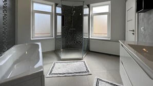 Ein modernes Badezimmer mit einer Glaskabine zur Dusche, einer freistehenden Badewanne und großen Fenstern für natürliches Licht.