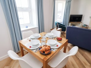 A dining area with a wooden table set for four, white chairs, and a blue sofa in the background. - Belle's View (Scarborough)