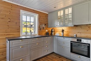 A kitchen with wooden walls, a window, grey cabinets, a sink, and an oven.