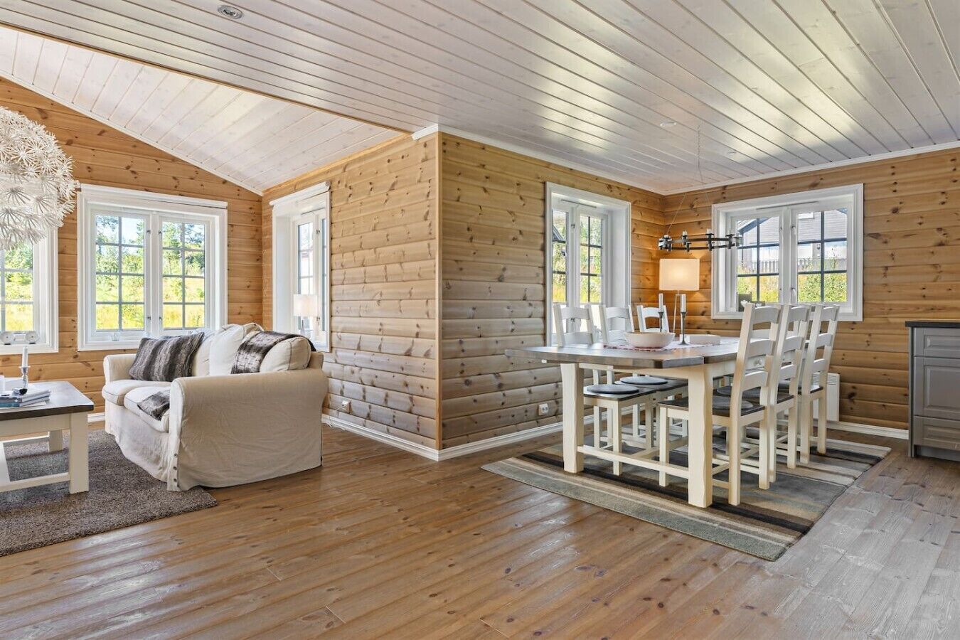 L’intérieur d’une cabane en rondins, avec un canapé, une table à manger, des chaises et une lampe.