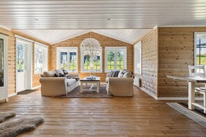 A log cabin interior with two sofas, a dining table, and a chandelier.