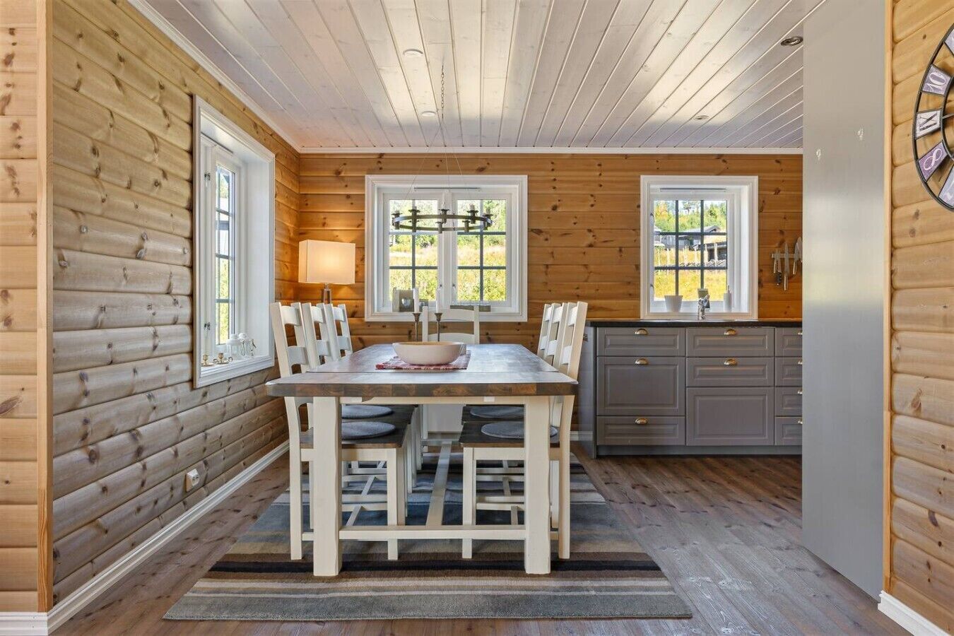 Un intérieur en bois comprenant une table à manger, des chaises, un coin cuisine et des fenêtres.
