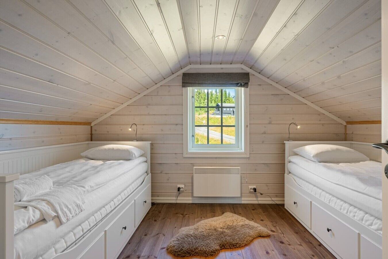 A room with two beds, a window, a radiator, and a wooden floor.