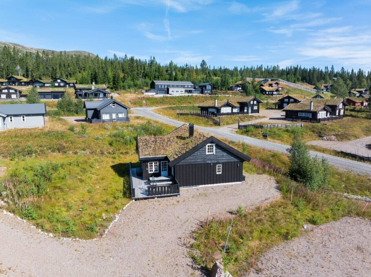 Un village rural avec des maisons traditionnelles en bois, une allée de gravier et un ciel dégagé.