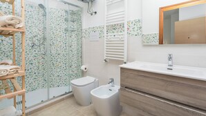 A bathroom with a shower, toilet, bidet, wooden shelf with towels, and a mirror. - Bed and Breakfast 'Sentiti A Casa' with Wi-Fi and Air Conditioning (Bronte)