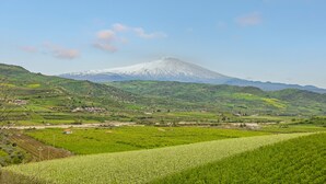 A mountainous landscape with a snow-capped peak, green fields, and scattered buildings. - Bed and Breakfast 'Sentiti A Casa' with Wi-Fi and Air Conditioning (Bronte)