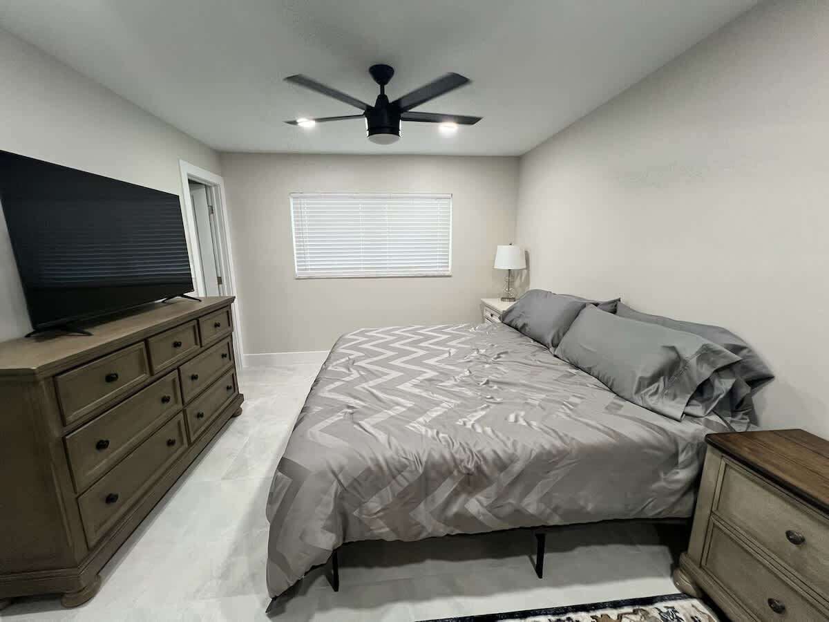 Een slaapkamer met een bed, een dressoir, nachtkastje, lamp, plafondventilator en een televisie op een dressoir.