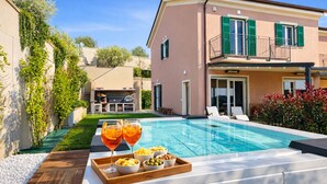 Une table à manger installée au bord de la piscine, avec deux verres de jus d’orange et des bols remplis de collations.