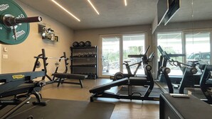 Une salle de sport équipée de matériel de musculation, de tapis de course et dotée d’un mur recouvert de miroirs.