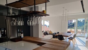 Une cuisine moderne avec un plan de travail en marbre, des verres à vin rangés sur un présentoir, et un coin repas comprenant une table et des chaises en bois.