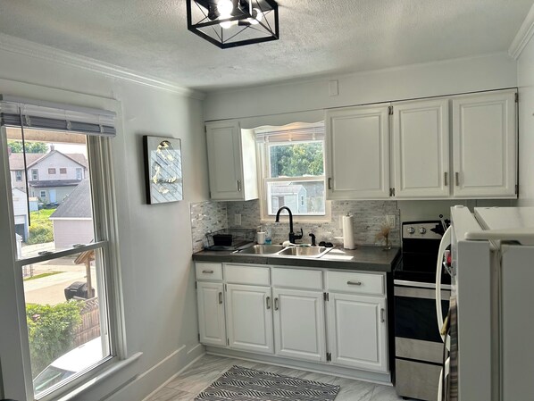 A kitchen with white cabinets, a black faucet, a window, and a patterned rug. - Charming studio with Office, Full Kitchen, strong WiFi, Washer, and Dryer (Dubuque)