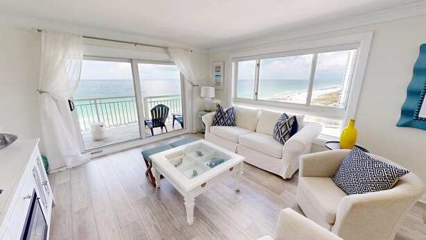 Ein geräumiges Wohnzimmer mit einem weißen Sofa, einem Glastisch und Blick auf den Strand.