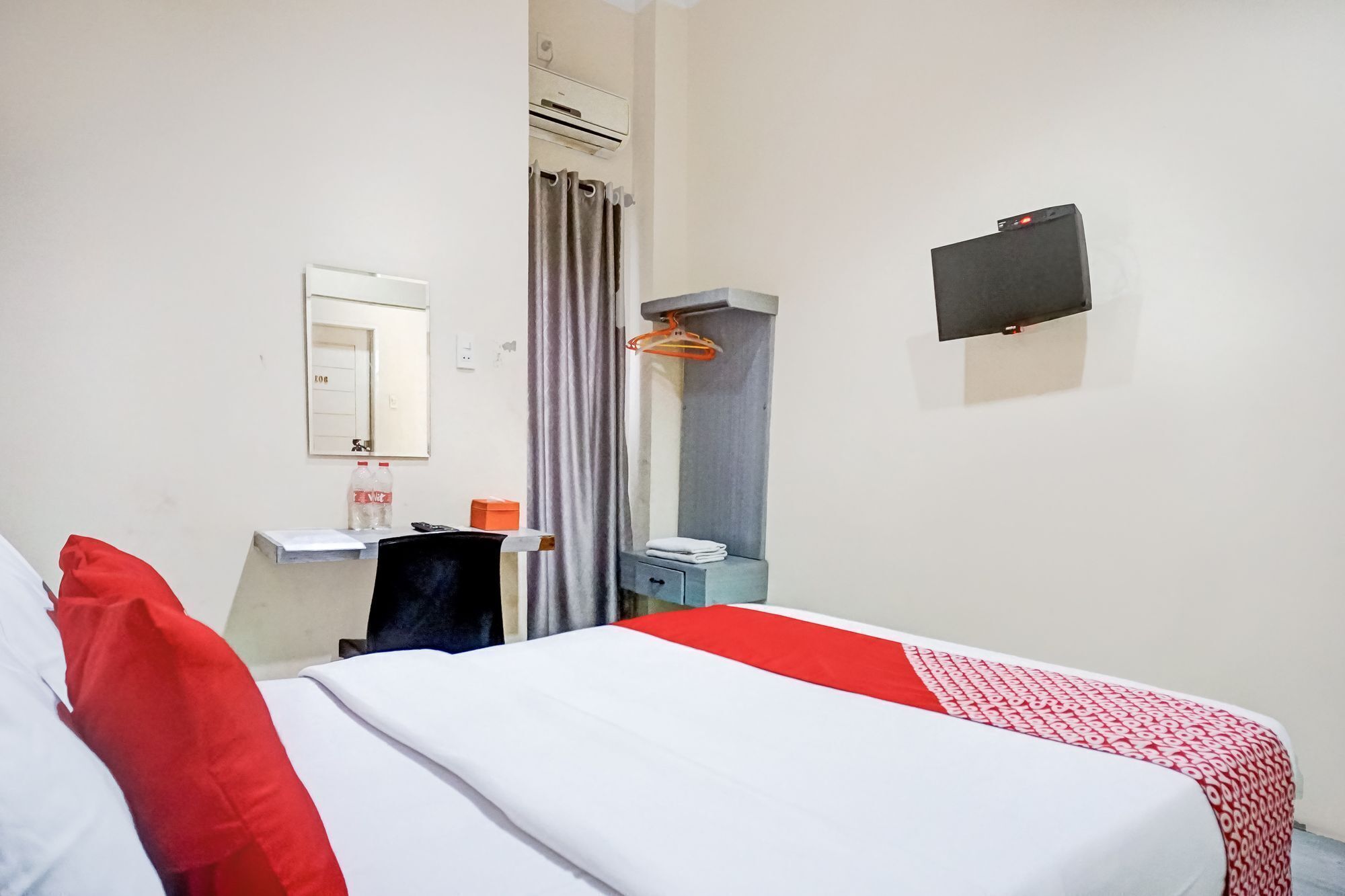 A hotel room with a bed, a desk, a mirror, a shower area, and a TV mounted on the wall.