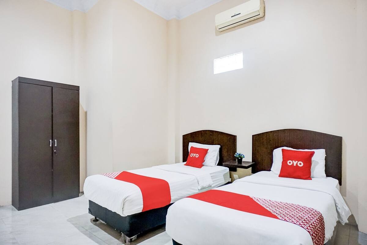 A hotel room with two beds, each with a red and white bedspread and matching pillows. There is a wardrobe and an air conditioning unit on the wall.