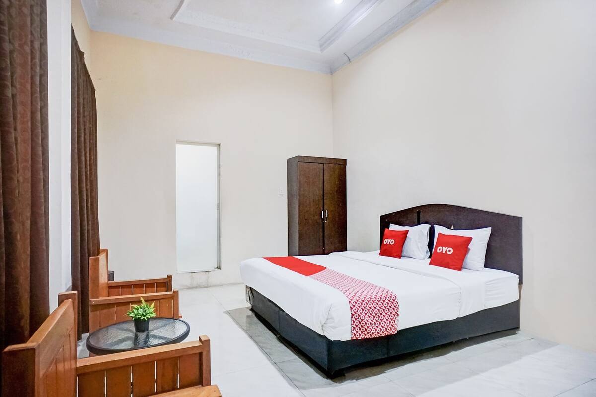 A bedroom with a bed, a wardrobe, a small table with a plant, and a chair.