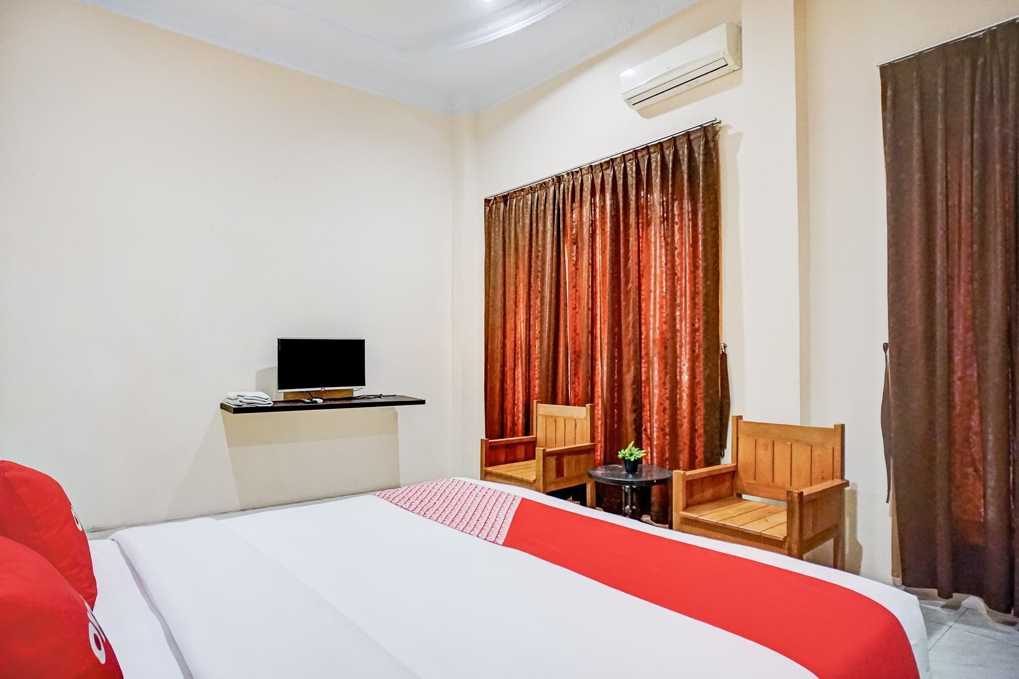 A hotel room with a bed, a desk with a computer, two chairs, and a small table with a plant.