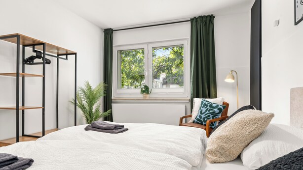 Et moderne soveværelse med seng, et sengebord, en lampe, et vindue med gardiner og en plante.