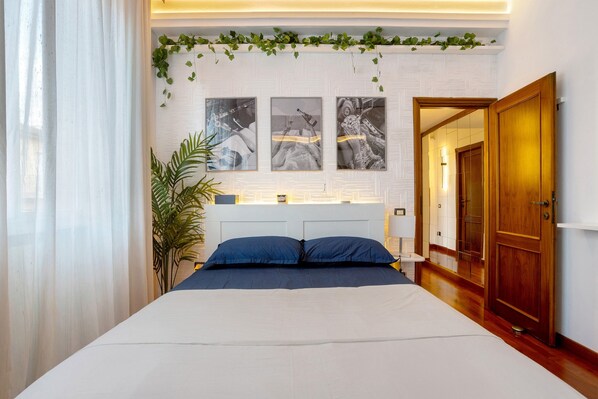 A bedroom with a bed, a bedside table, a nightstand, a wooden door, and a wall with three framed pictures.