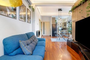 A modern living room with a blue sofa, a flat-screen TV, and a kitchen in the background.