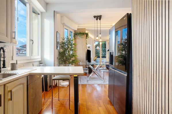 Una cocina moderna con una isla central, electrodomésticos de acero inoxidable y un comedor con una escalera que lleva a un nivel superior.