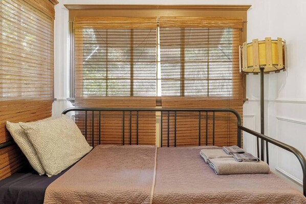 Una habitación con una cama, una ventana con mosquitera y una lámpara.