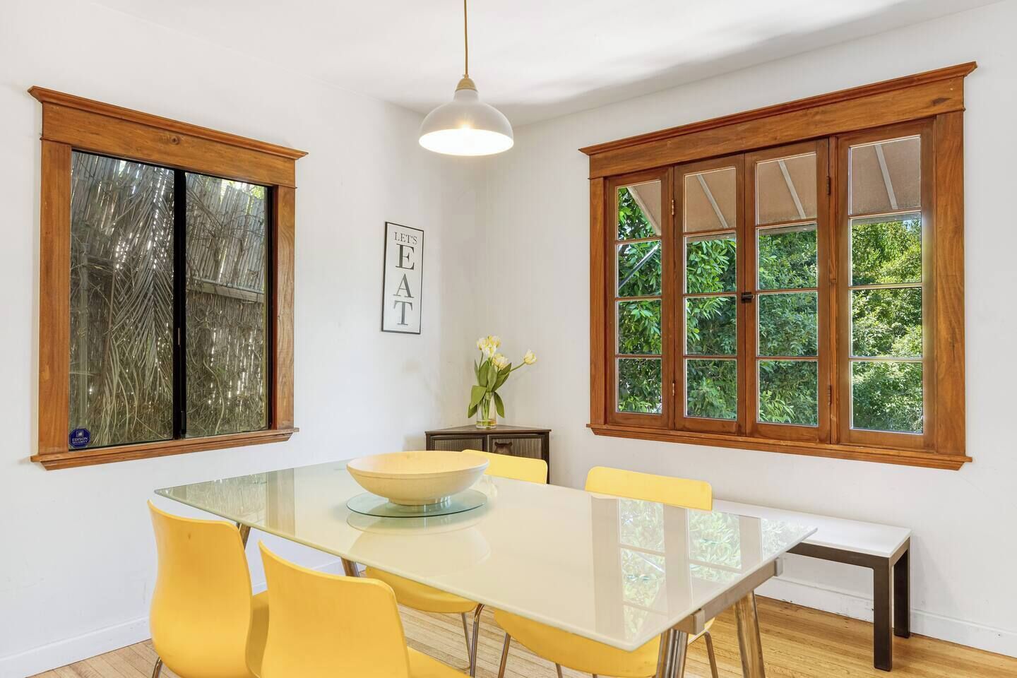 A dining area with a large table, yellow chairs, a bowl, and a vase with flowers.
