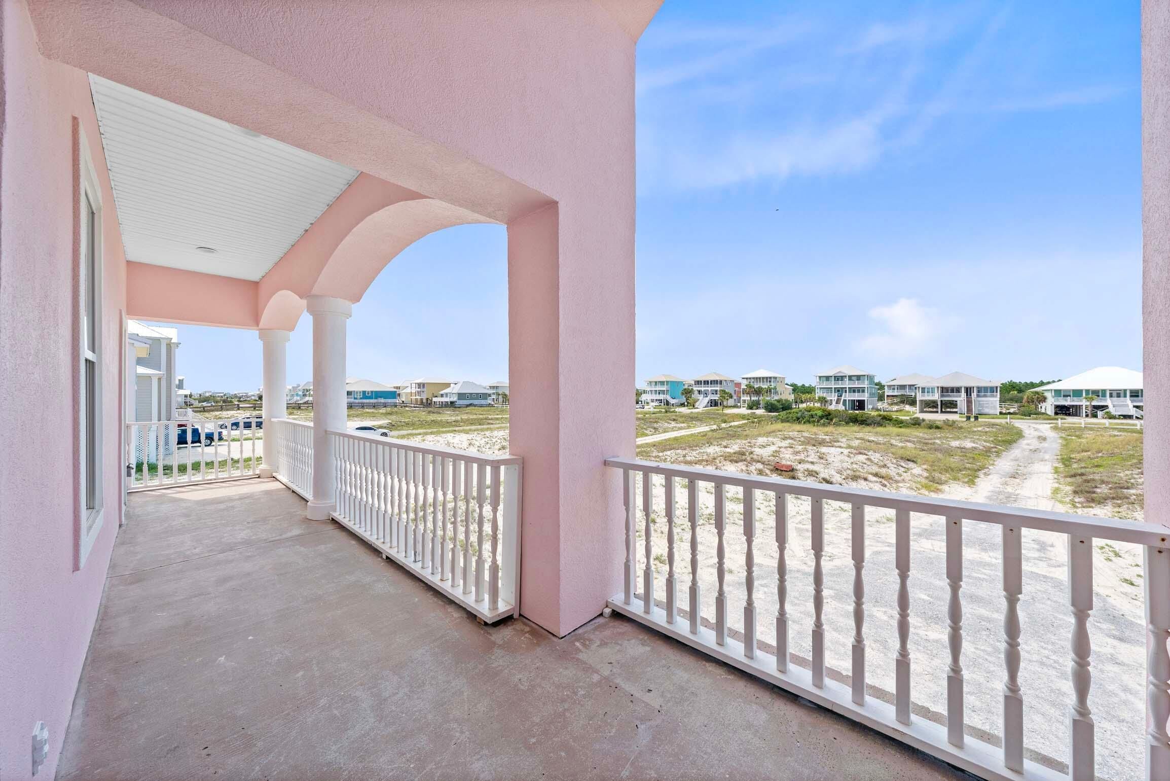 A balcony with a view of a sandy beach and buildings in the distance.