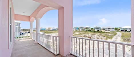 A balcony with a view of a sandy beach and buildings in the distance.