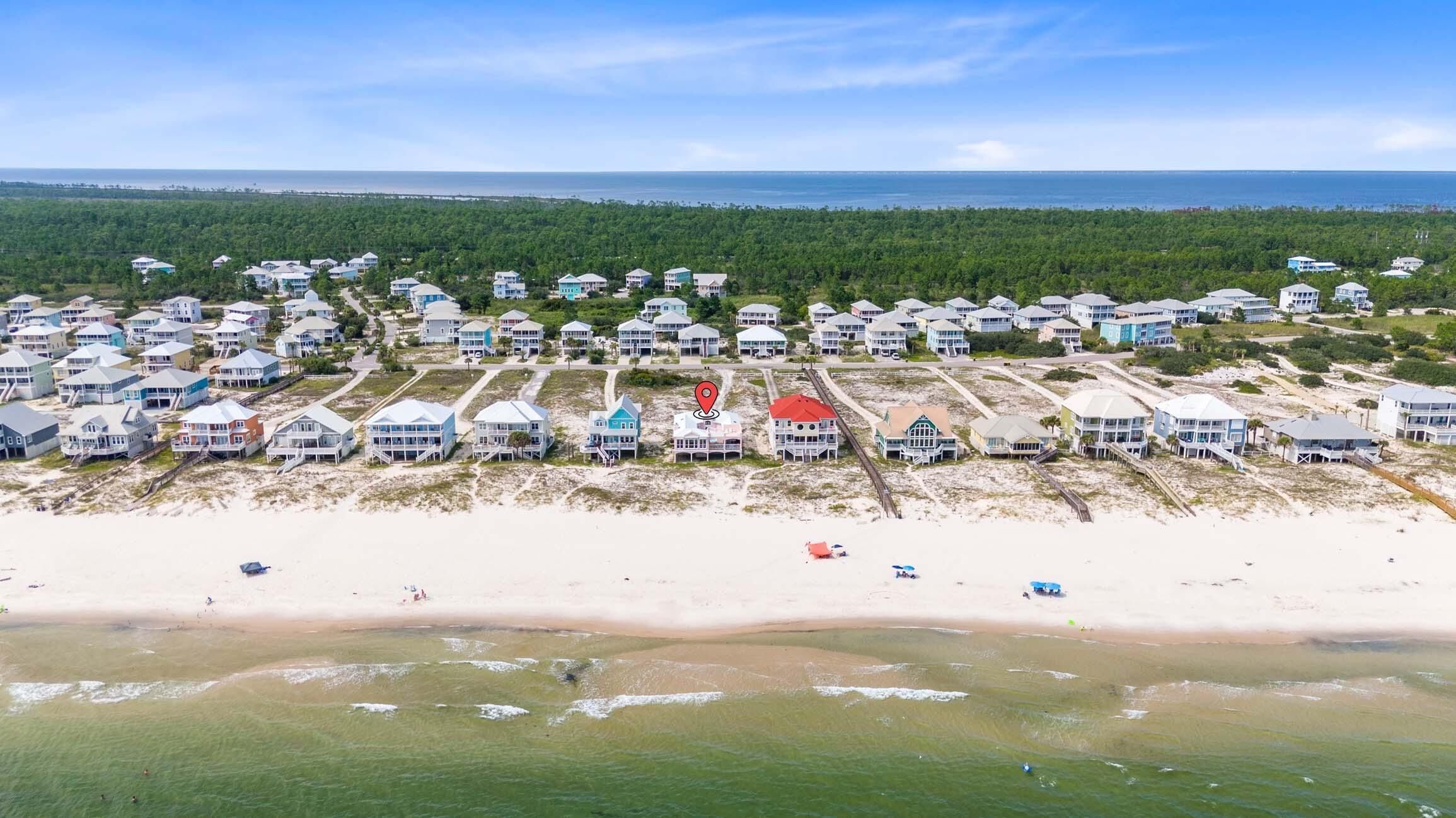 An aerial view of a coastal residential area with beachfront properties, a sandy beach, and a distant view of the ocean.
