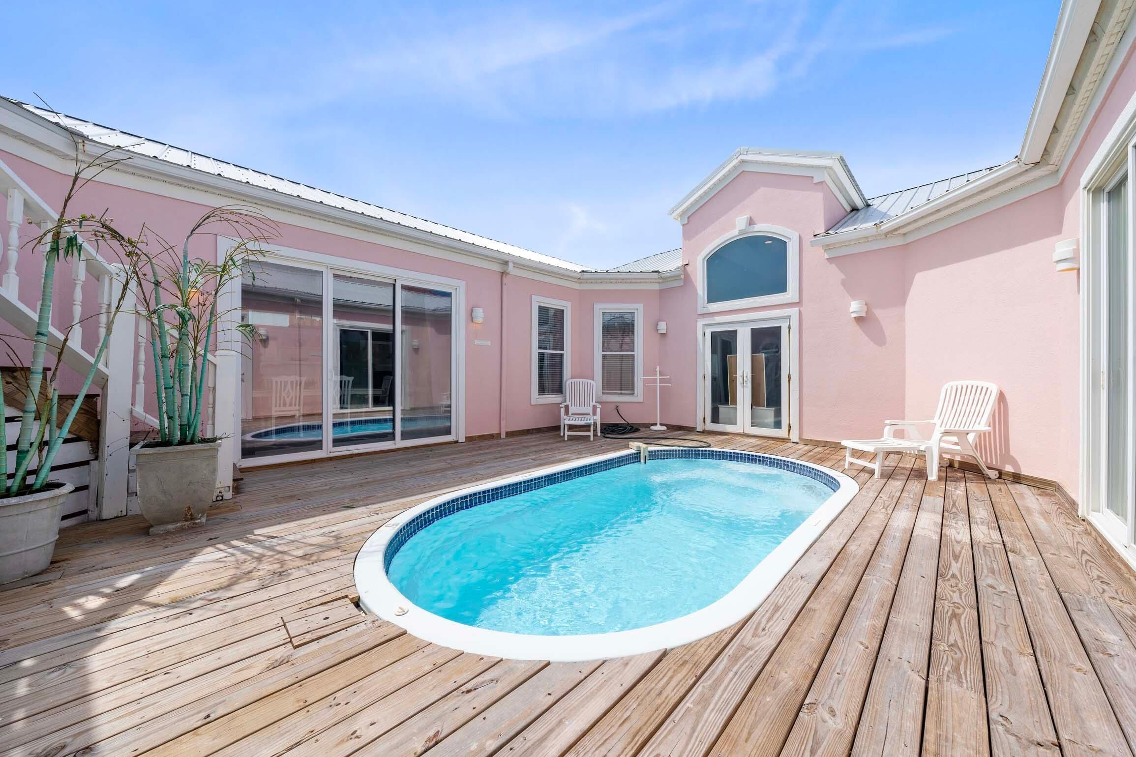 A wooden deck with a swimming pool, white chairs, and potted plants.