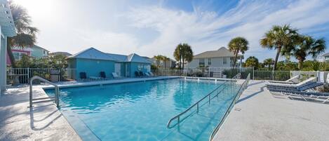 A swimming pool with a clear blue water, surrounded by a concrete deck and lounge chairs.