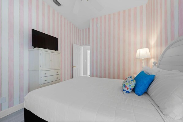 A bedroom with a bed, a TV on a dresser, and a door leading to another room. - Candy Land (Gulf Shores)