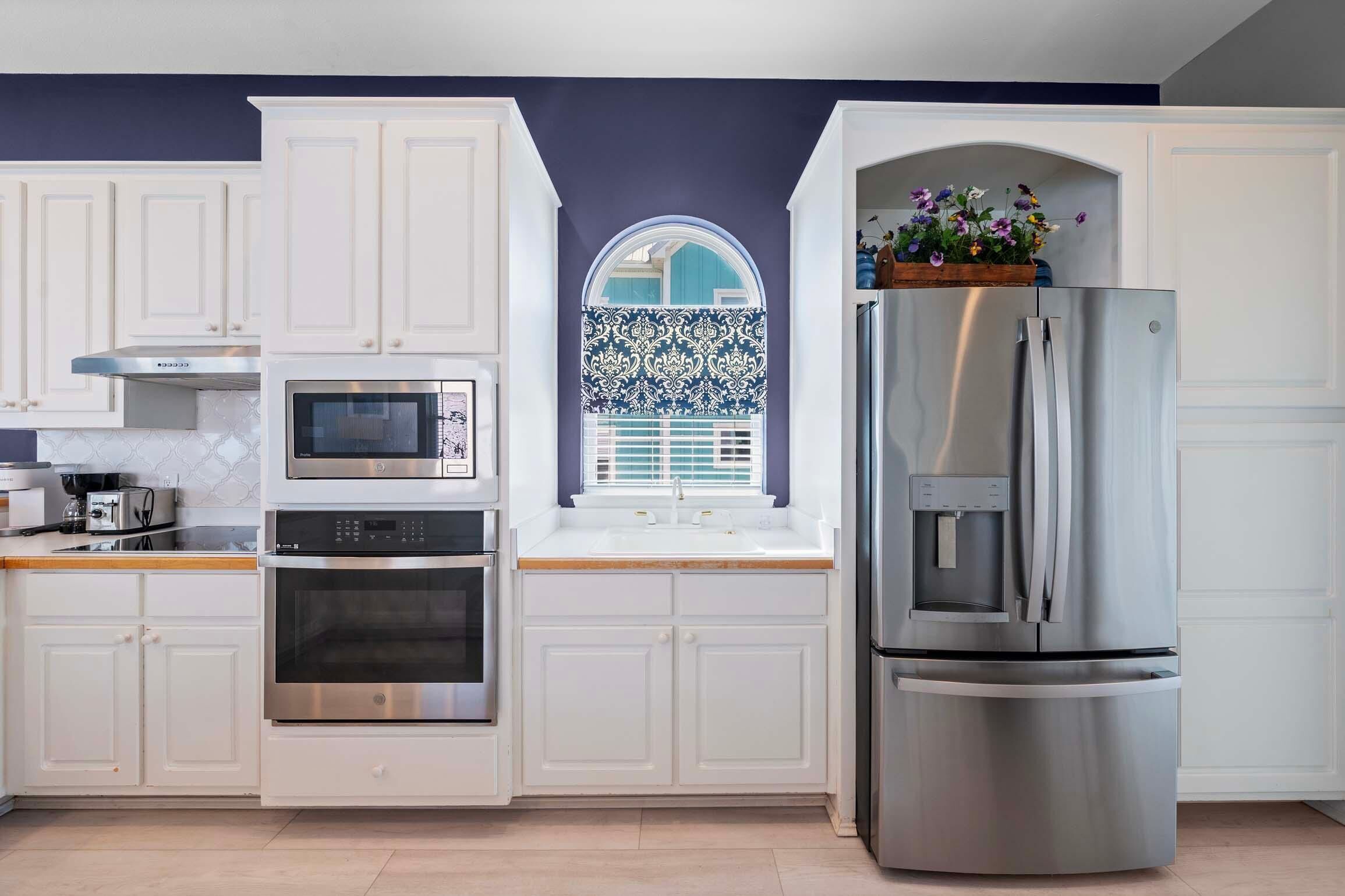 Een moderne keuken met witte kastjes, roestvrijstalen apparatuur en een raam met een decoratief blauw-wit patroon.