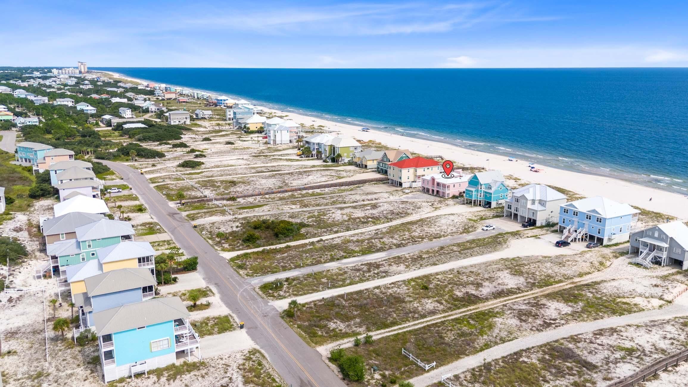 Una zona residencial costera con casas a lo largo de la playa, una carretera y vista al océano.