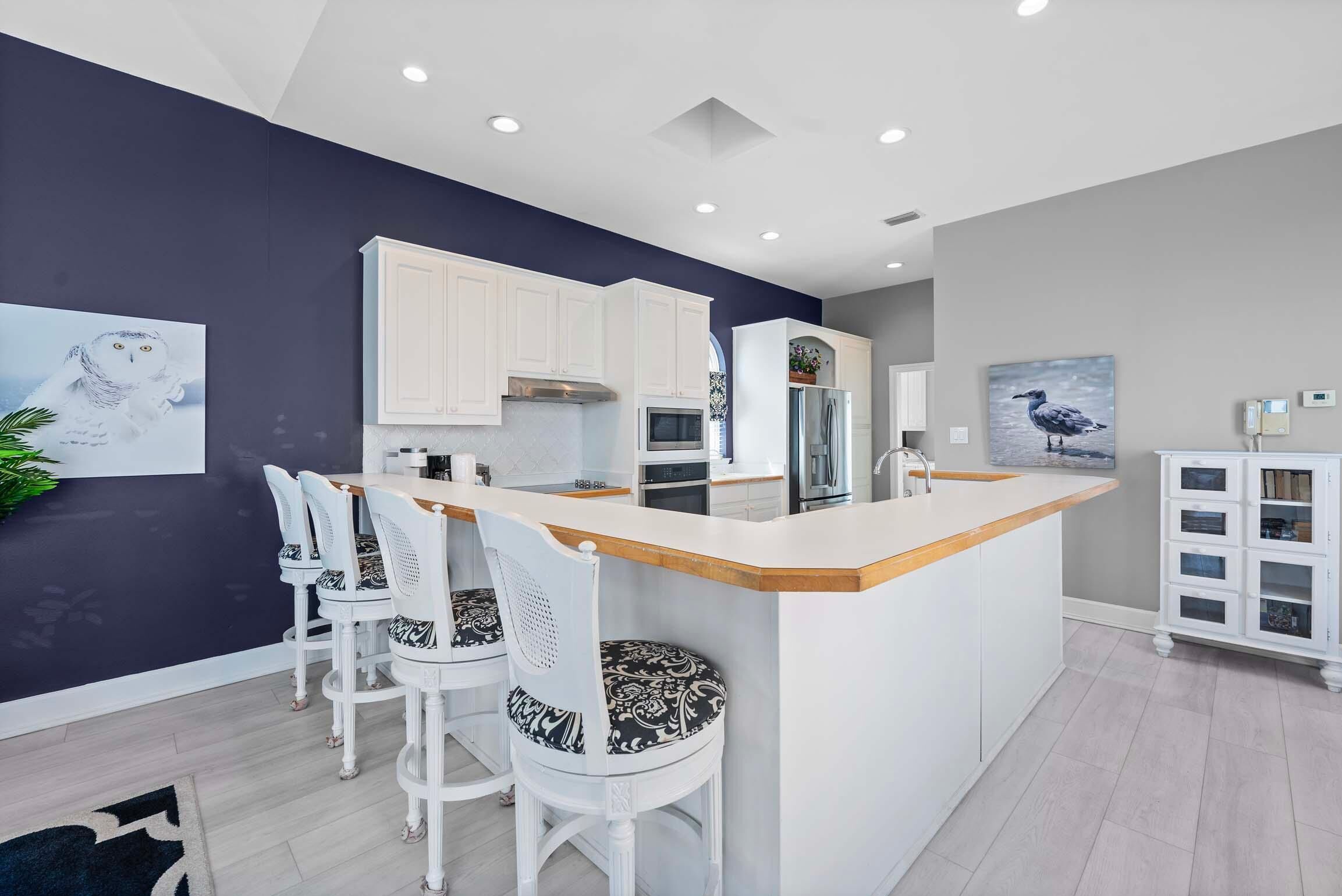 A modern kitchen with white cabinets, a central island with bar stools, and artwork on the walls.