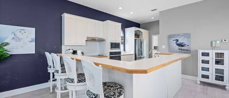 A modern kitchen with white cabinets, a central island with bar stools, and artwork on the walls.