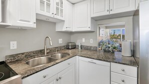 A modern kitchen with white cabinetry, granite countertops, a Bosch dishwasher, and a view of the outdoors. - 2/2 Canal front condo, Pool, Beach Access (Longboat Key)