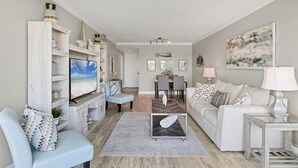 A living room with a TV, a sofa, a coffee table, and a dining area with chairs and a table. - 2/2 Canal front condo, Pool, Beach Access (Longboat Key)