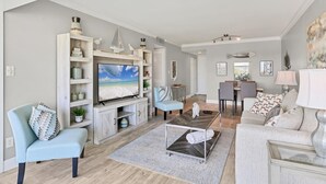 A modern living room with a flat-screen TV, light blue armchairs, a coffee table, and a dining area with a table and chairs. - 2/2 Canal front condo, Pool, Beach Access (Longboat Key)