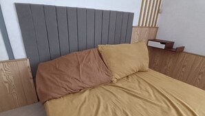 Ein Bett mit grauem Kopfteil, Holzbeschlägen und einer beigen Matratze.