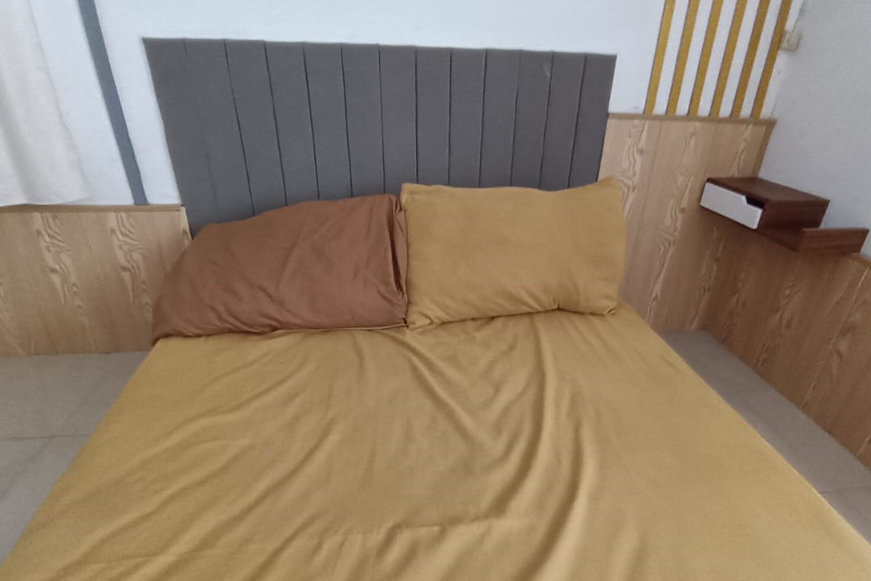 A bed with a grey headboard, two pillows, and a wooden nightstand with a drawer.