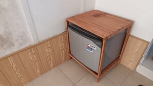 Ein kleiner, holzrahmenverkleideter Kühlschrank mit Aufkleber an der Tür, platziert in einer Ecke mit Holzvertäfelung und Fliesenboden.
