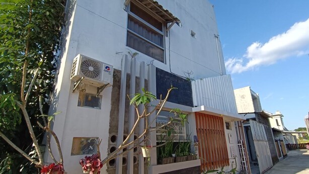 Ein weißes Gebäude mit einer großen Klimaanlage, einem Fenster mit Holzklappe und einem kleinen Balkon mit Pflanzen.