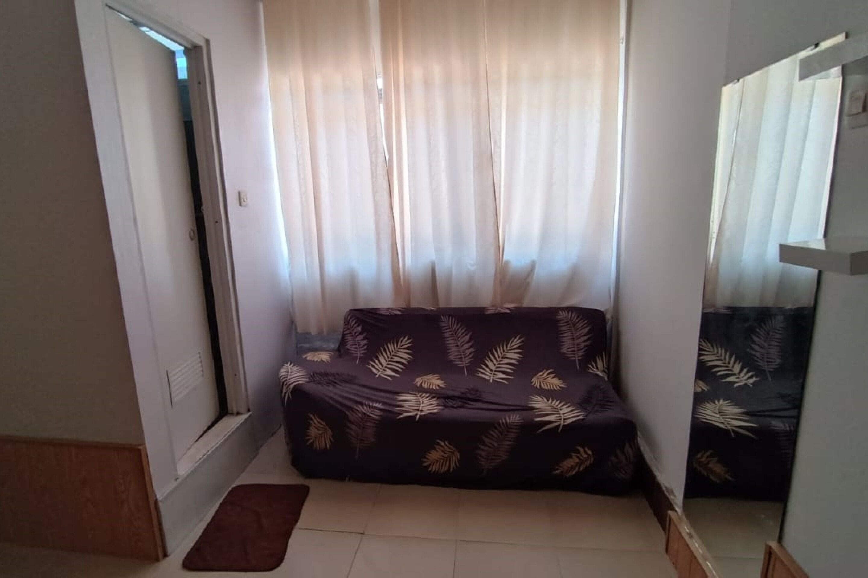 A room with a sofa, a window with sheer curtains, and a door.