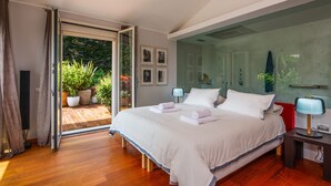 A bedroom with a large bed, a glass door leading to a balcony, and a nightstand with a lamp.