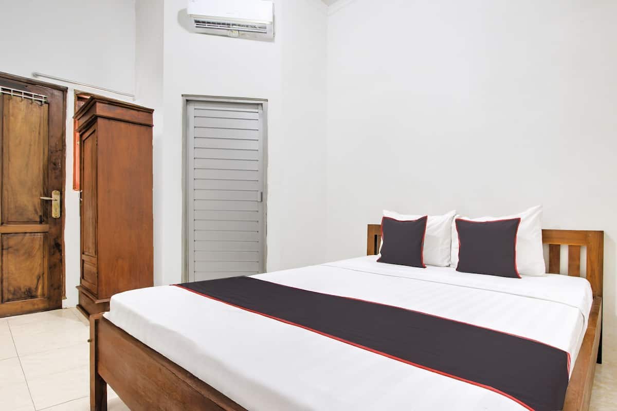 A bedroom with a wooden bed, white bedding, and a red and black accent.