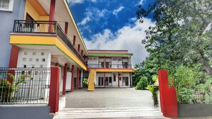 A two-story building with a balcony on the upper floor, a paved walkway leading to the entrance, and a fenced garden area. - Hotel O Oteng Stay (Semarang)